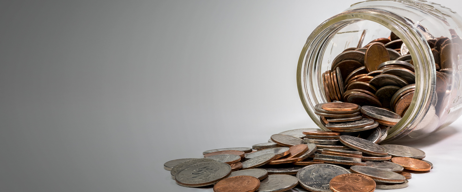 A clear glass jar lying on it's side with loose change spilling out of it.