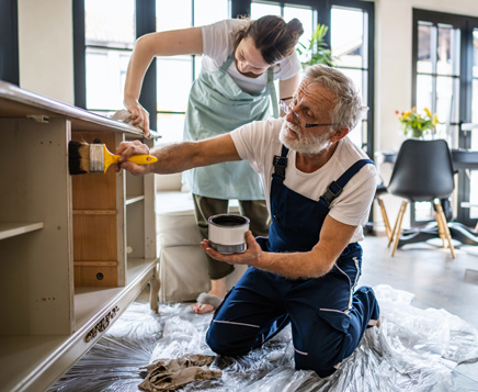 Husband and wife painting cabinets in kitchen.
