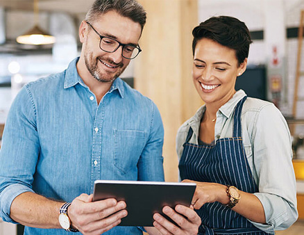 Business owners smiling while looking at tablet going over finances.