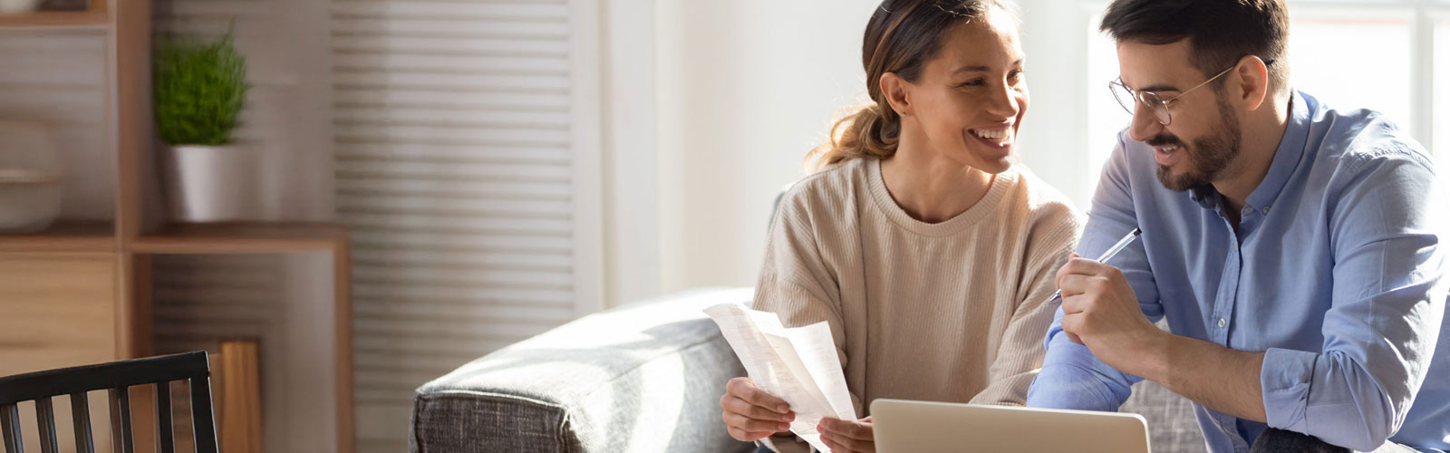 A smiling couple going over documents and finances on their laptop.
