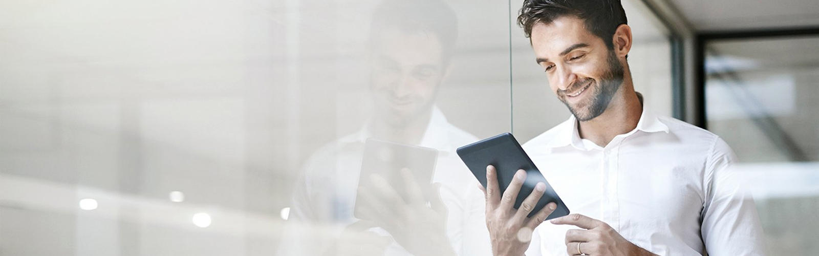 A happy man leaning against a window while looking at his banking on his mobile device.