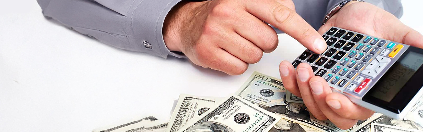 Hand typing on a calculator with various denominations of money scattered about.