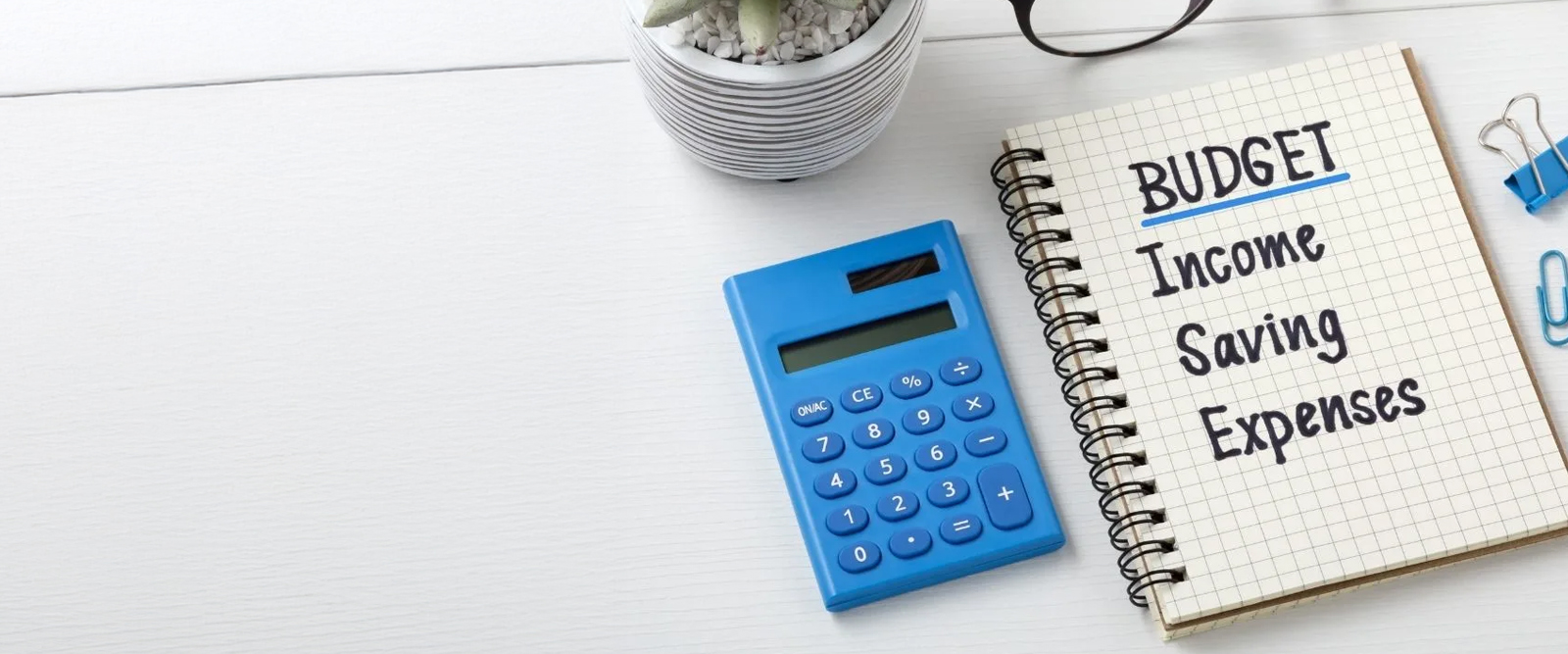 A calculator next to a note pad with the outline of a budget written on it.