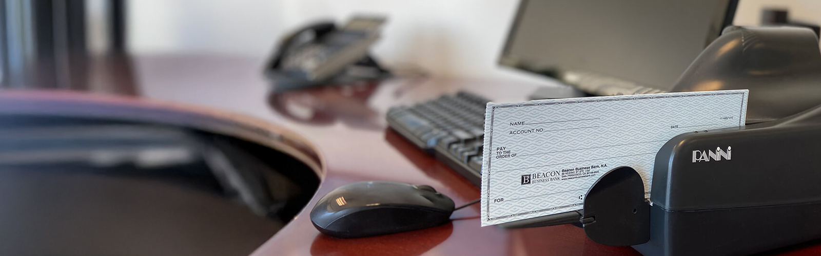 Photo of a work desk with a computer and a check scanner with a check loaded and ready to be scanned.