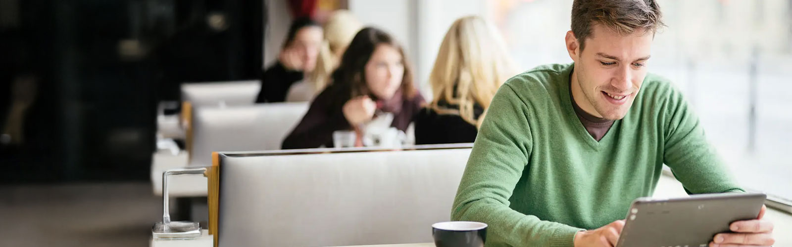 Photo of young man sitting in a coffee shop on his tablet.