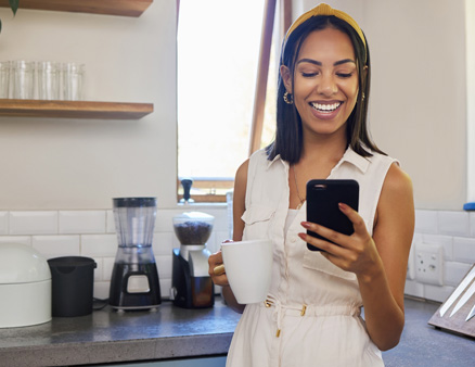 Young woman smiling while using phone in kitchen.