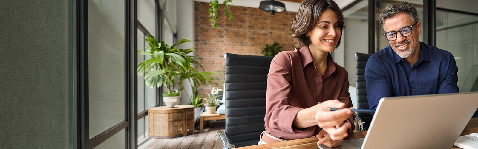 Business people smiling while looking at payroll records on a laptop.
