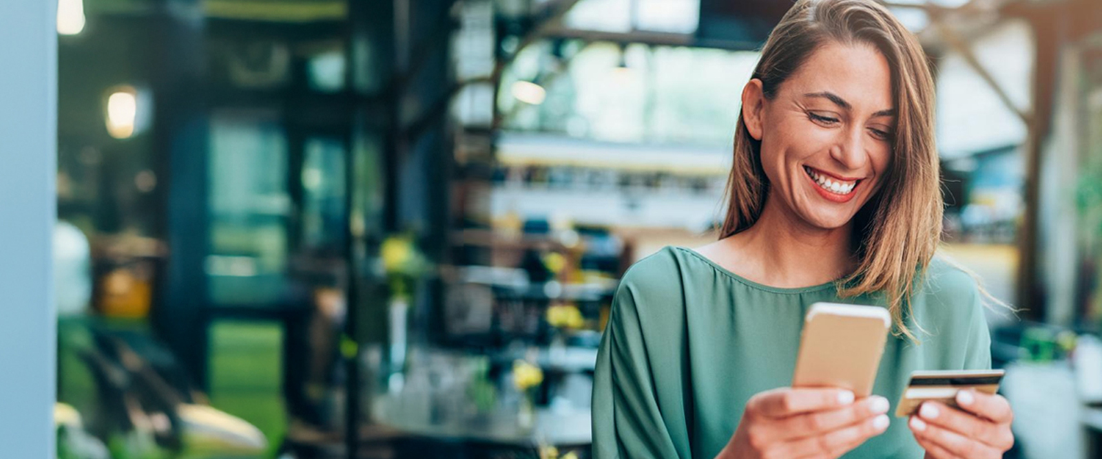 Woman smiling while holding her phone and debit card as she does her banking digitally.